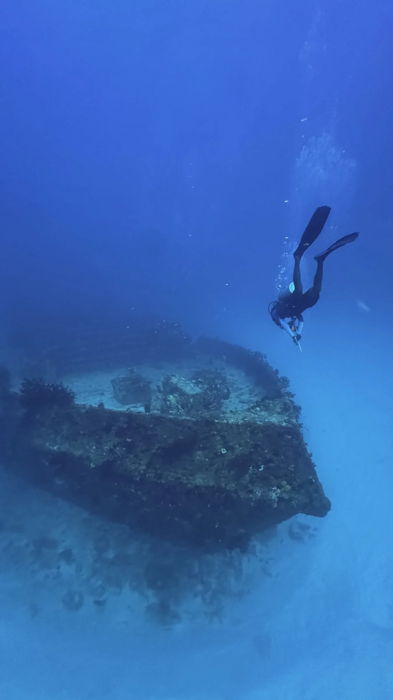 A diver passes above the wreck in clear blue water.