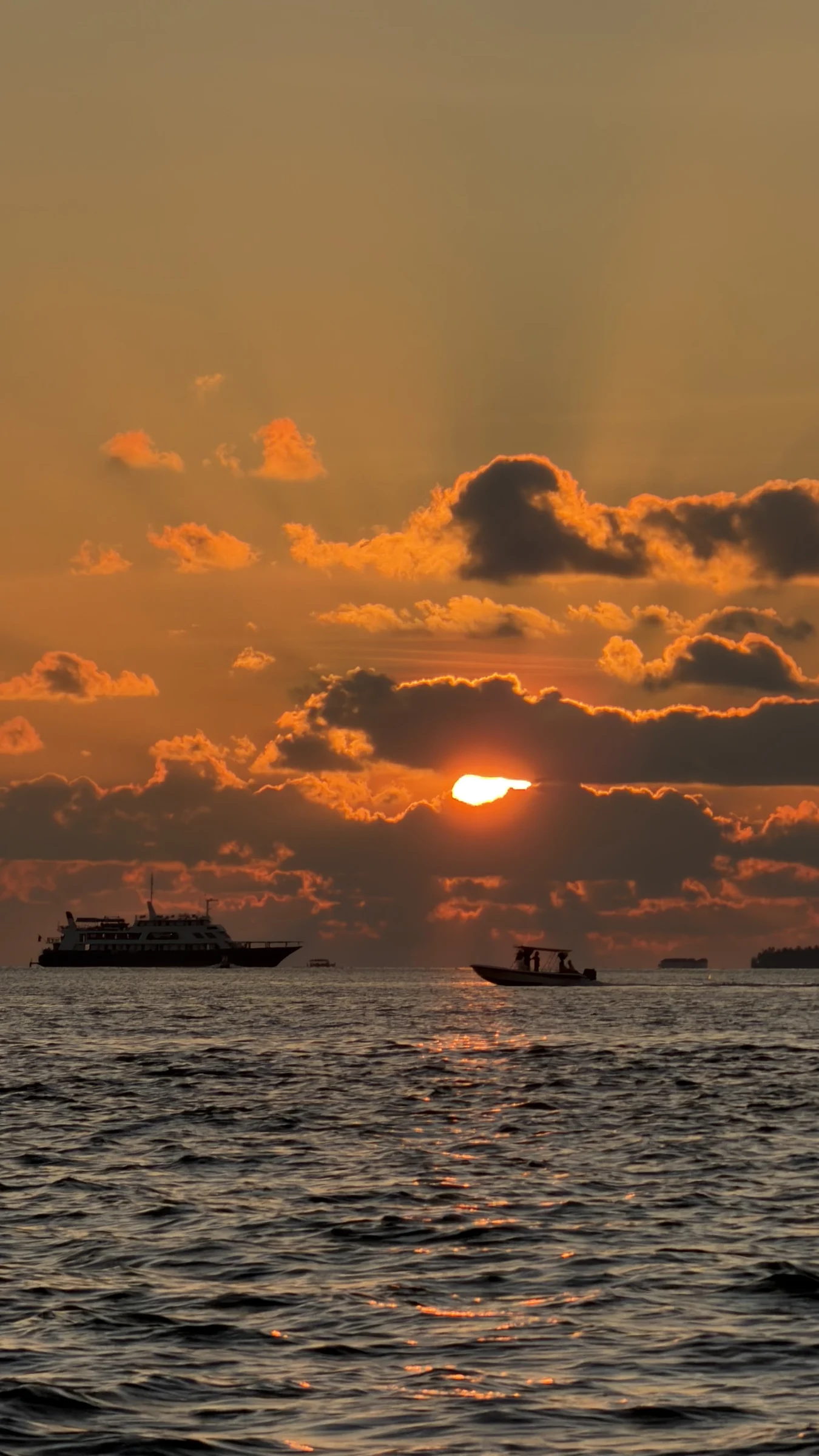 Boats cross the glowing horizon at sunset.